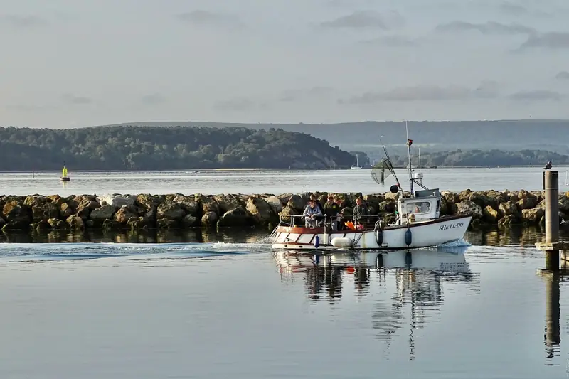 A fishing boat passing a rock breakwater at a harbour entrance