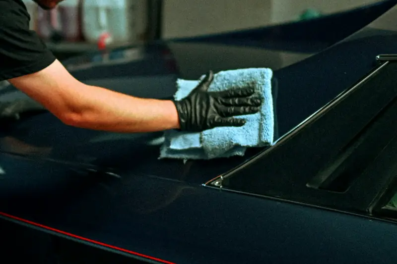 A gloved hand wiping a dark car panel with a microfibre cloth