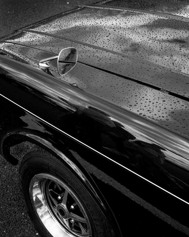 Water beading on the wing of a glossy black classic car