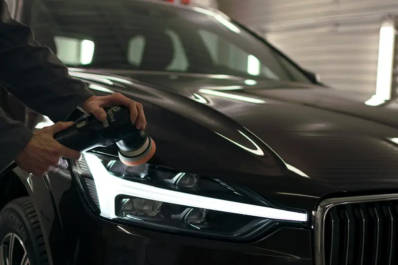 A detailer machine polishing the bonnet of a dark car next to its headlight