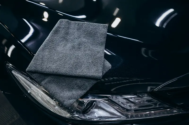 A grey microfibre towel resting on a glossy black car by its headlight